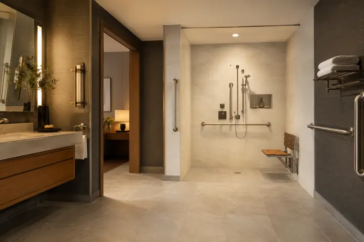 Accessible hotel bathroom with shower chair, grab bars, and adjustable mirror